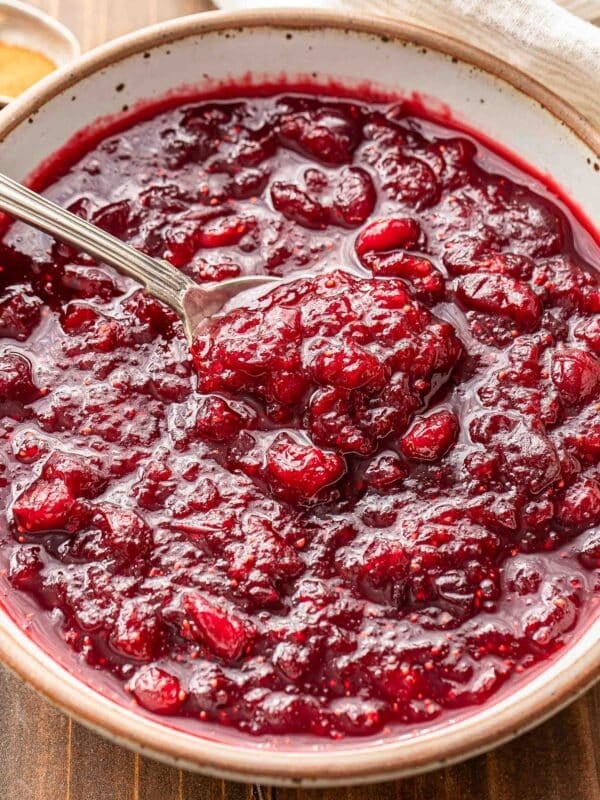 A white bowl with cranberry sauce and a spoon in it.