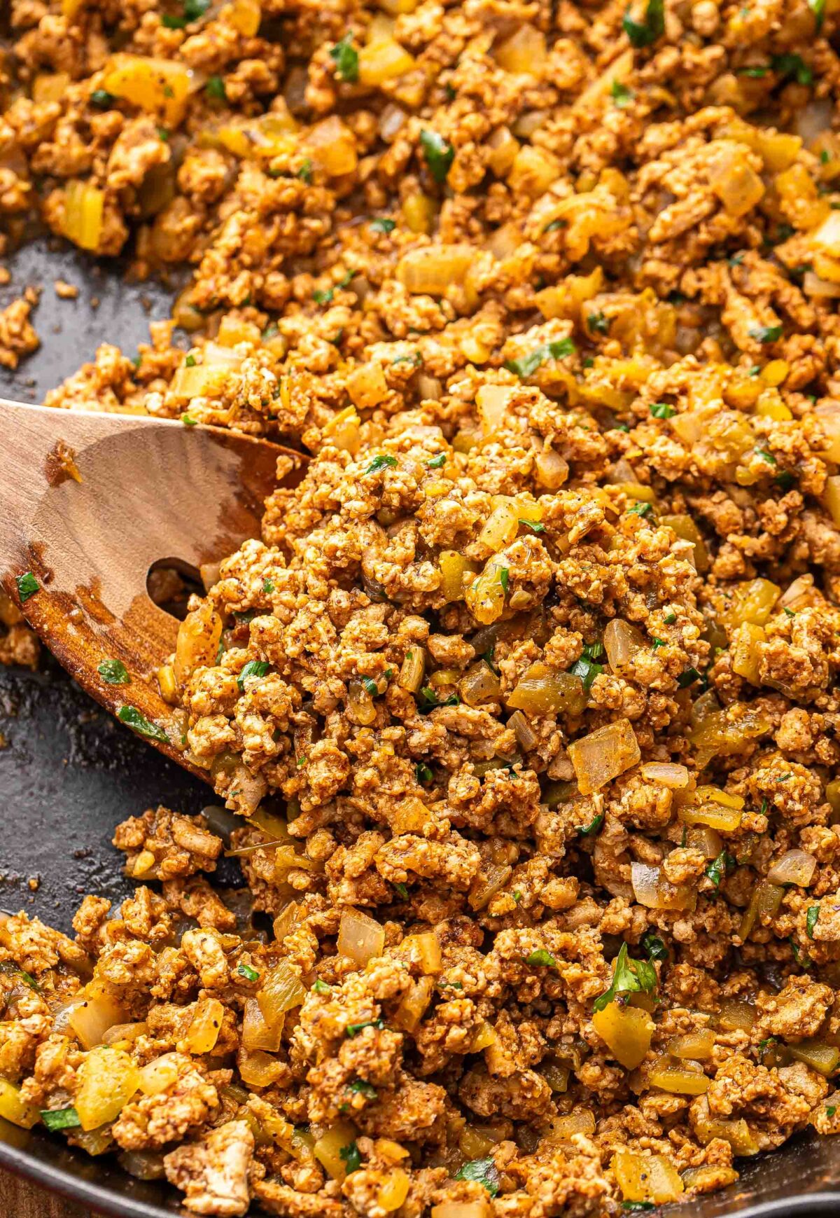 Wooden spoon scooping up turkey taco meat in a skillet.