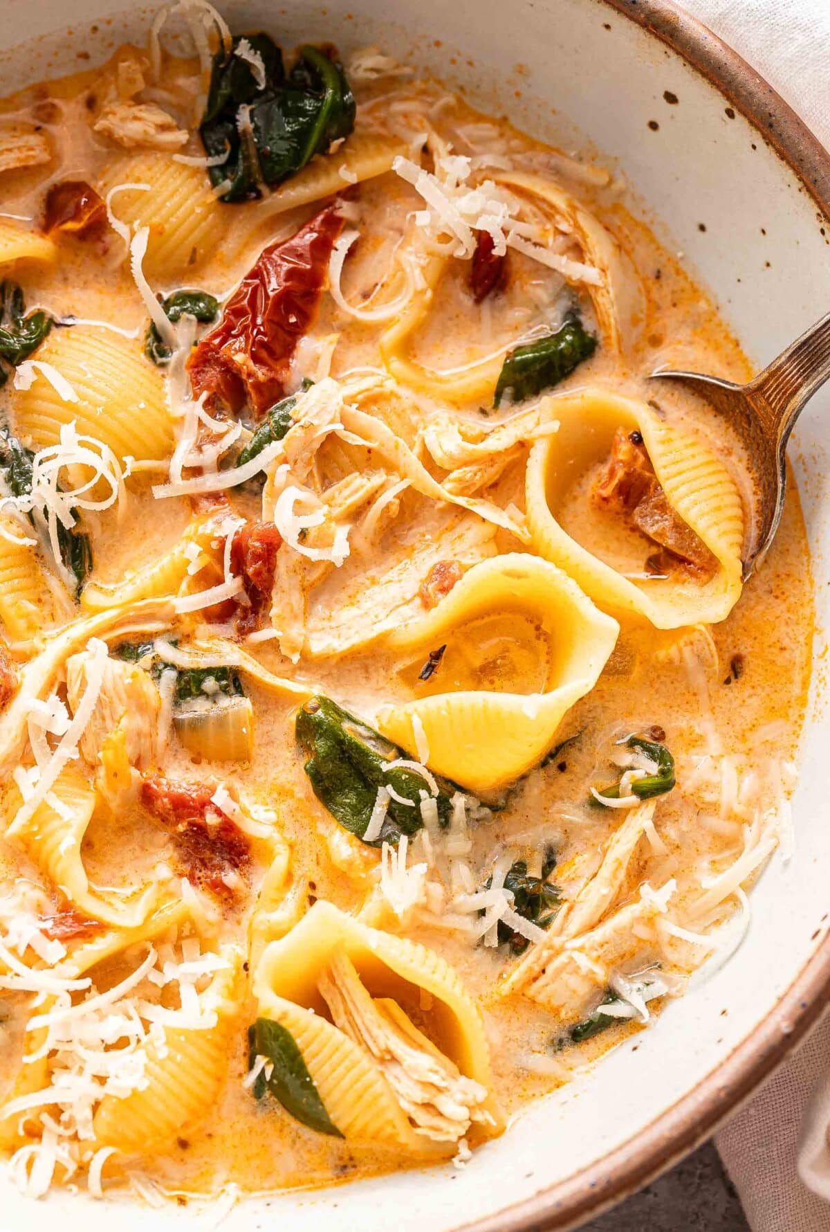 A white bowl with marry me chicken pasta soup and a spoon in it.