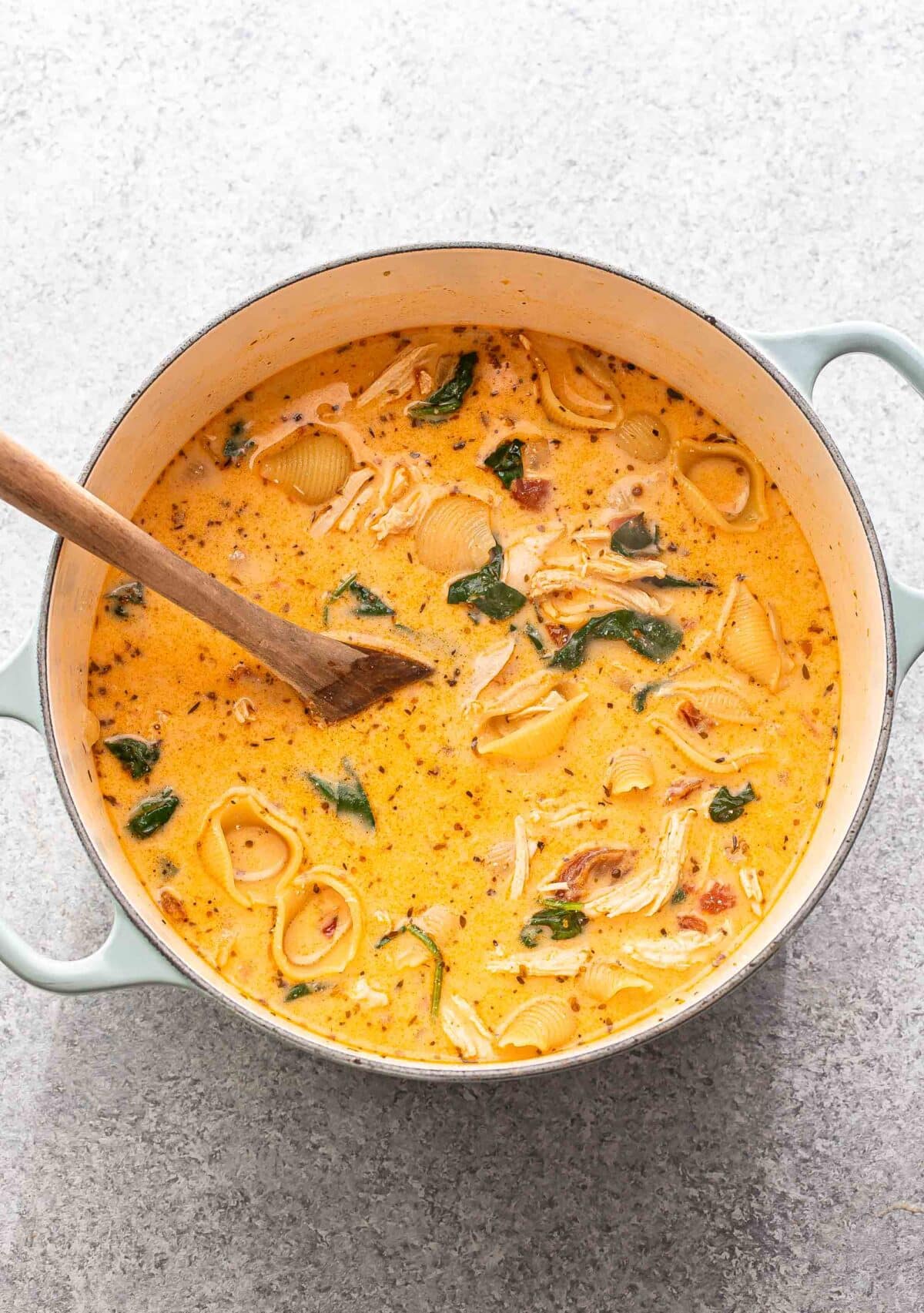 Creamy marry me chicken soup in a pot with a wooden spoon.