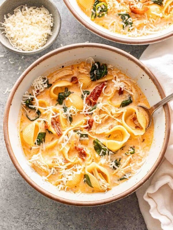 A white bowl with marry me chicken soup and a spoon in it. A bowl of parmesan cheese is behind the bowl.