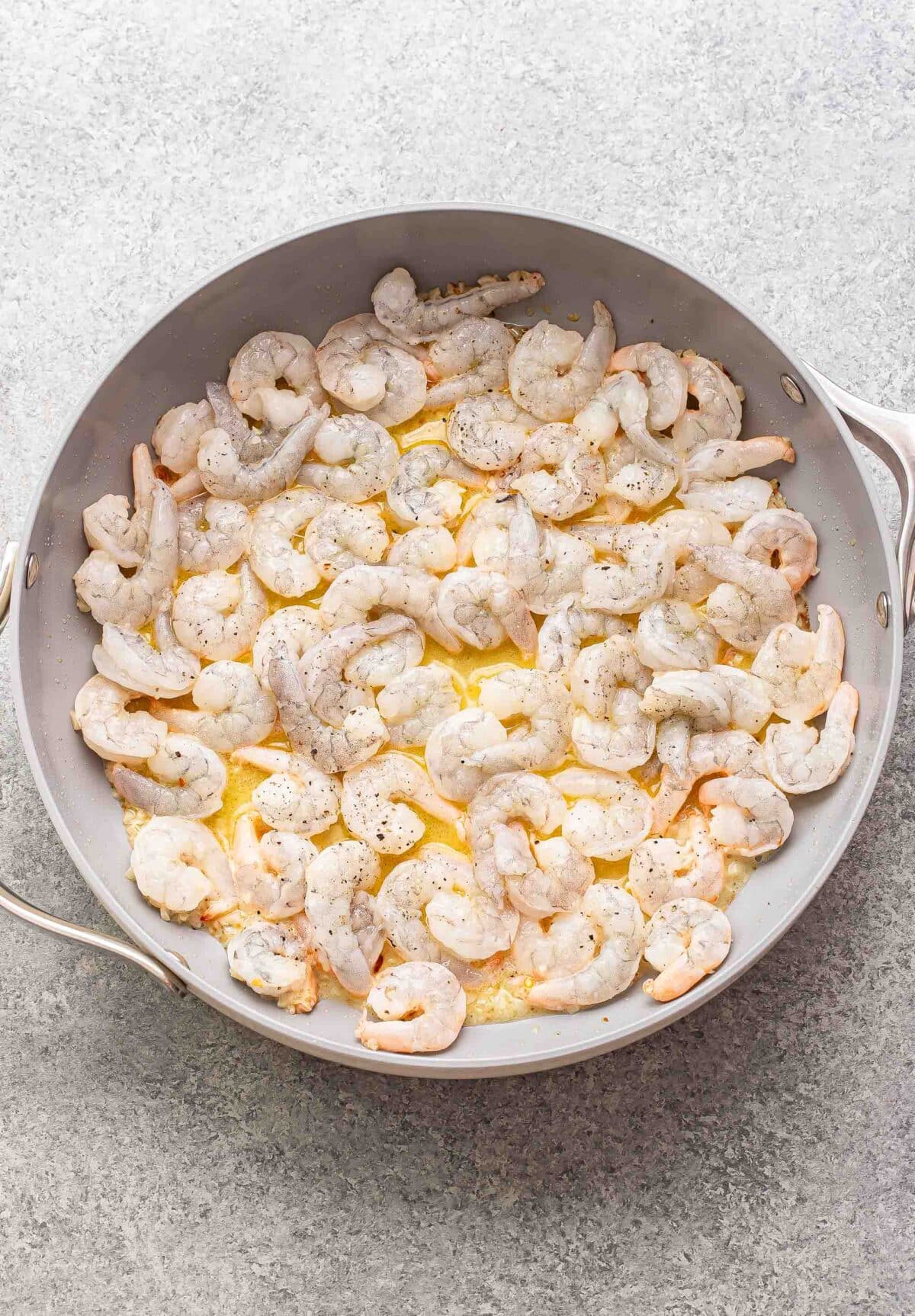 Uncooked shrimp in a skillet with melted butter, galric and white wine.