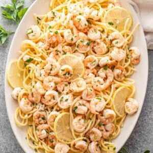 Shrimp scampi on top of pasta on an oval serving platter.