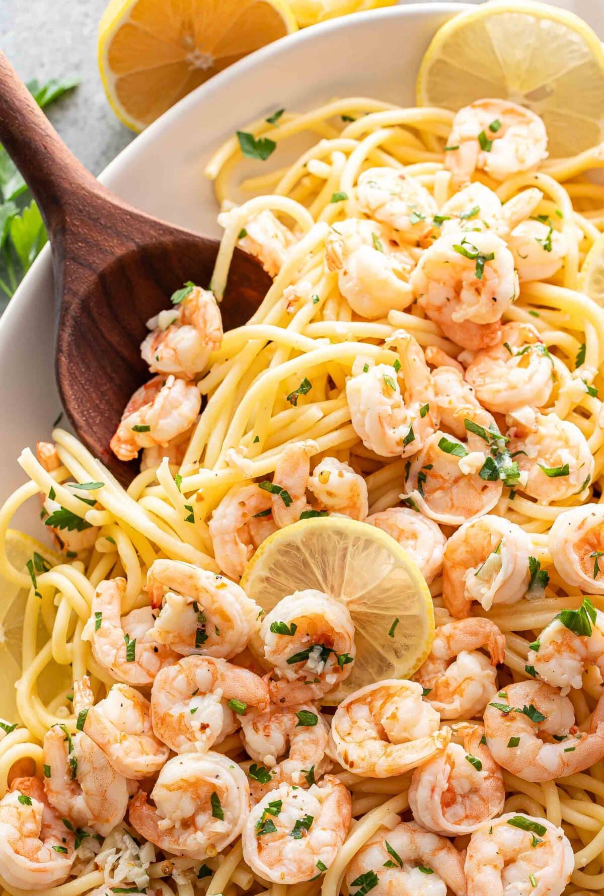 Shrimp scampi on top of pasta with a wooden serving spoon.