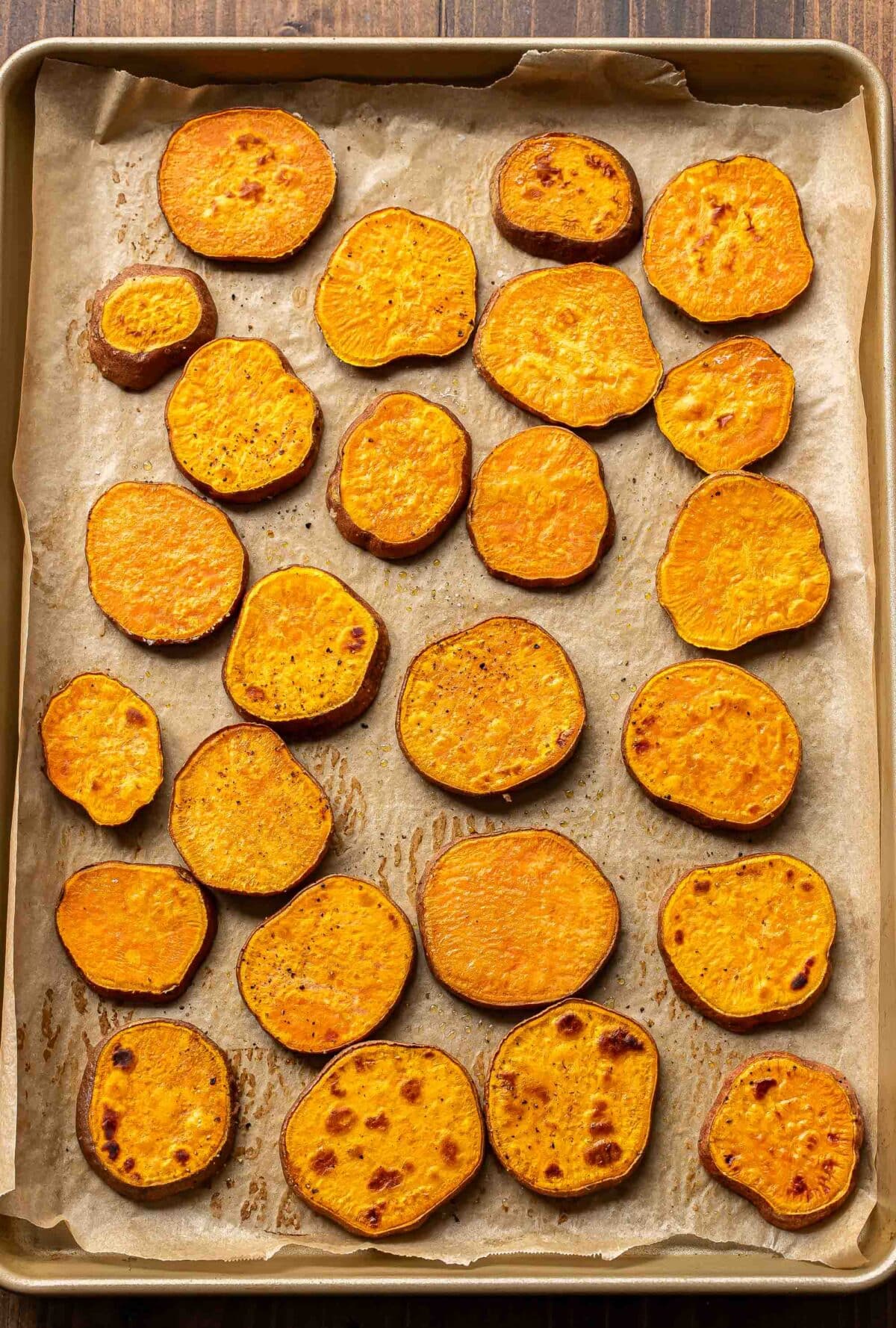 Roasted sweet potato rounds on a parchment paper lined sheet pan.