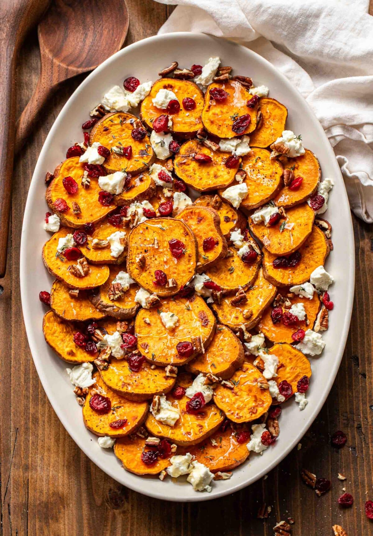 Roasted sweet potatoes on an oval platter with goat cheese crumbles, dried cranberries, and pecans.