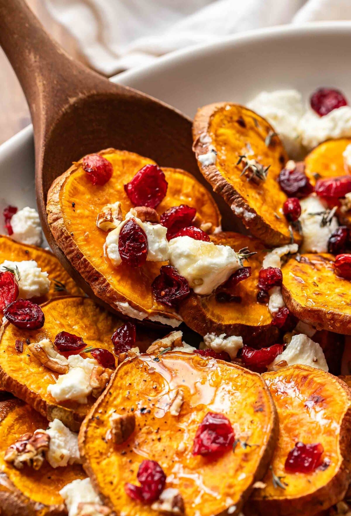 Wooden serving spoon scooping up sweet potato rounds with goat cheese, dried cranberries, and pecans.