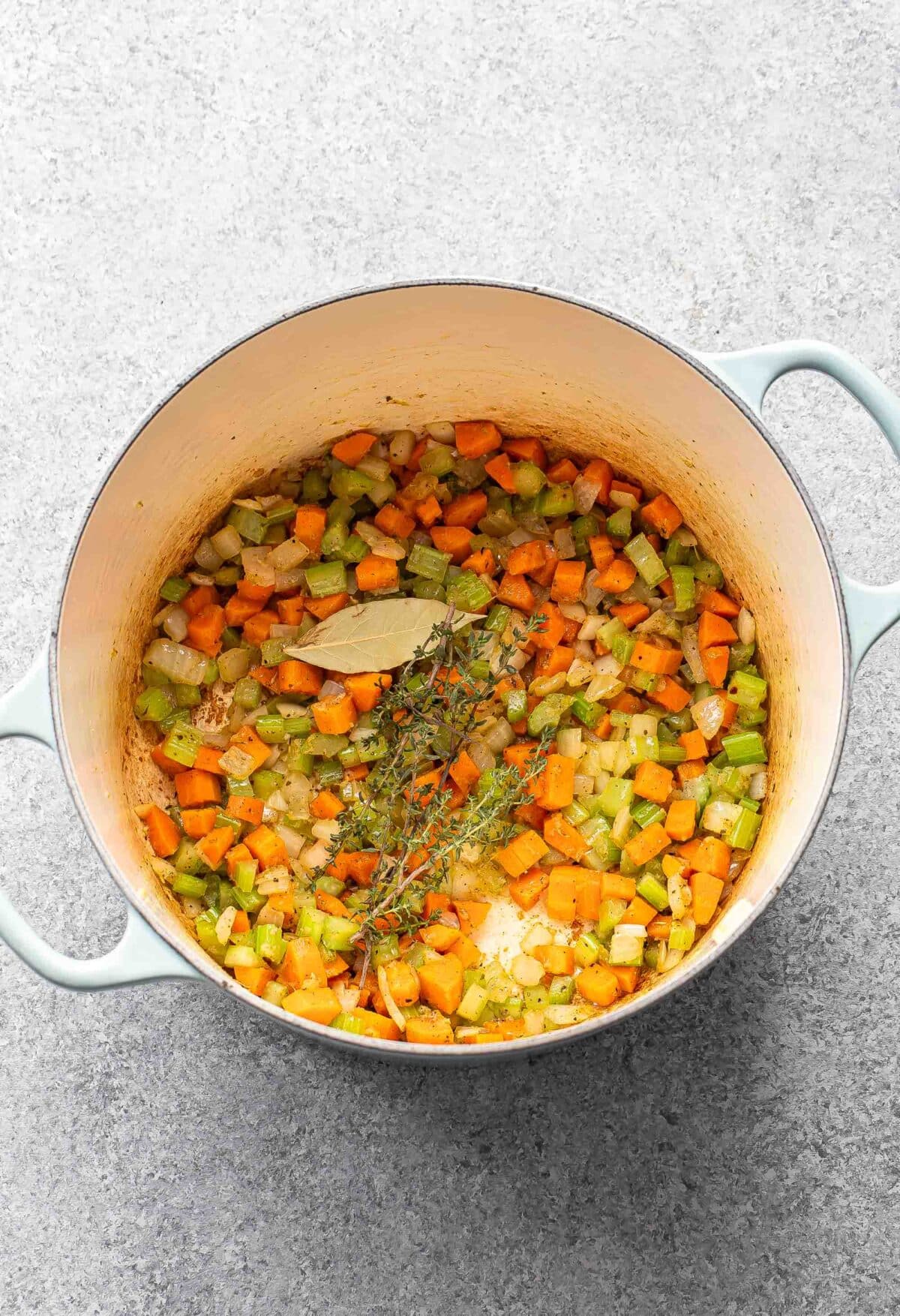 Carrots, celery, onion, thyme, and a bay leaf in a pot.