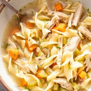 A white bowl with turkey noodle soup in it.