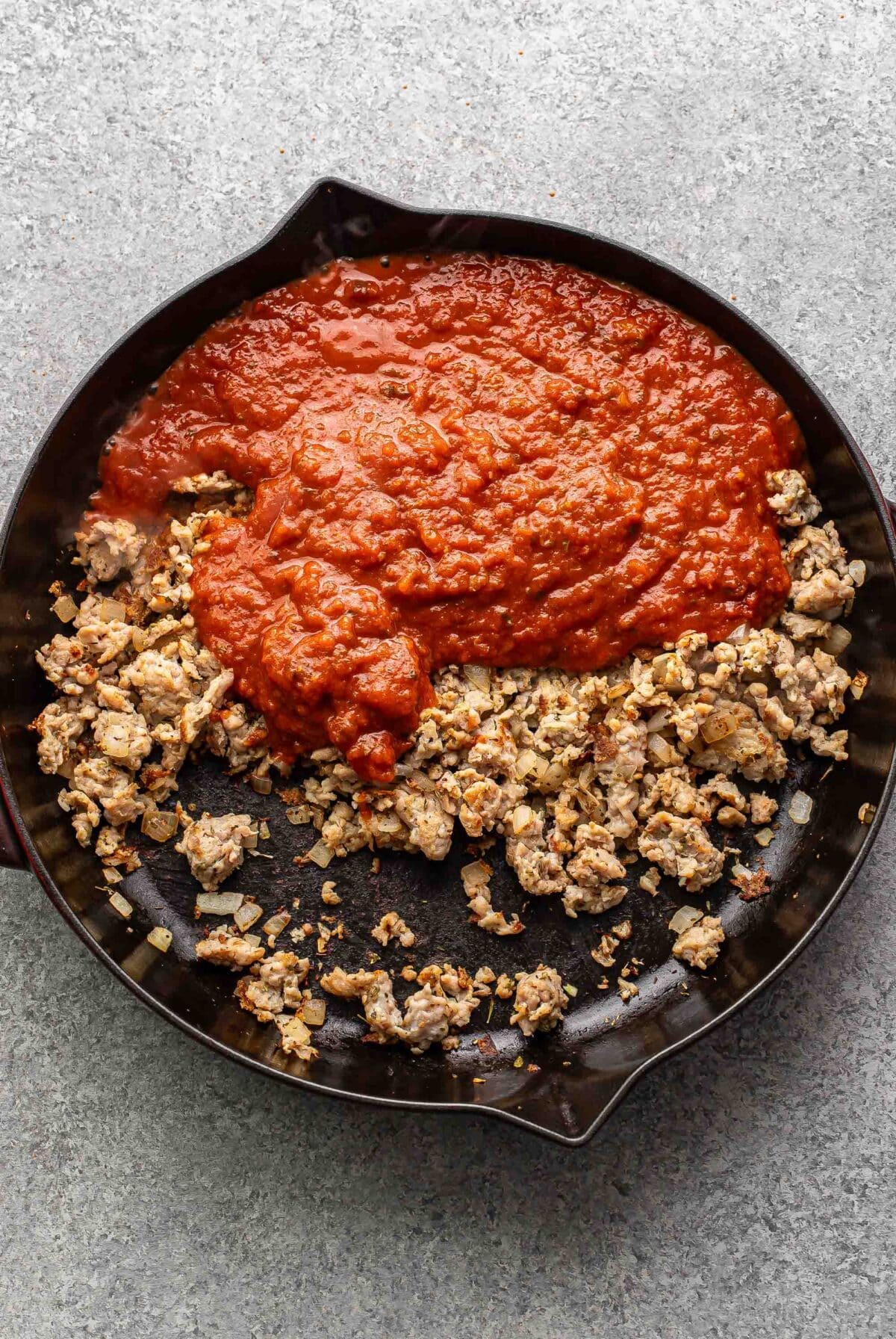 Crumbled Italian sausage with marinara sauce on top of it in a skillet.