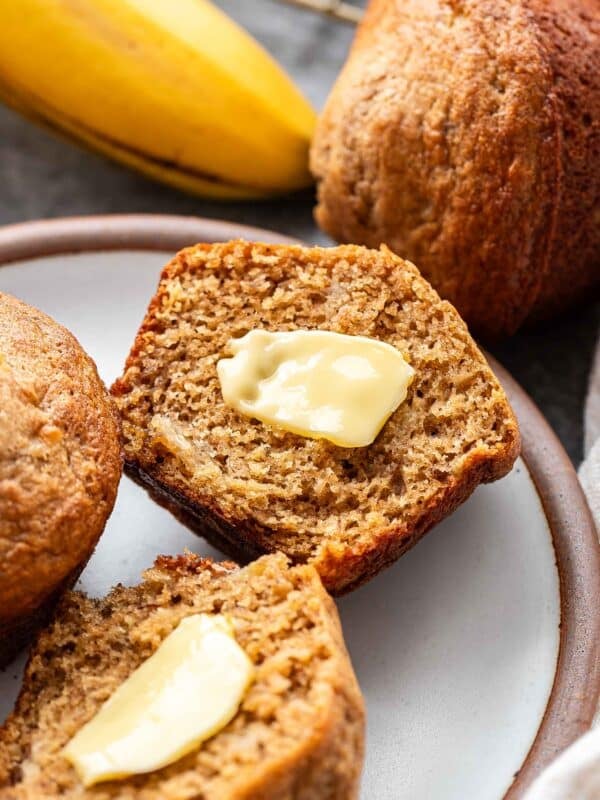 A banana muffin that's cut in half with butter on it on a white plate.