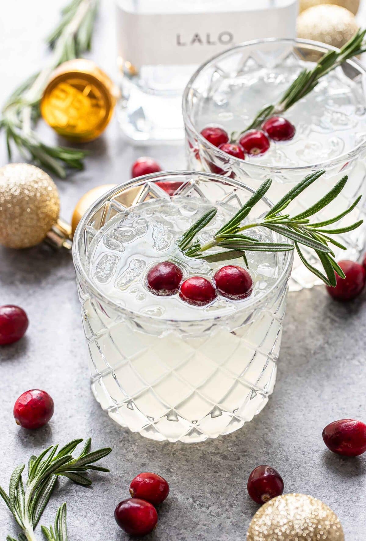 White cranberry christmas margarita in a glass garnished with a sprig of rosemary and fresh cranberries.