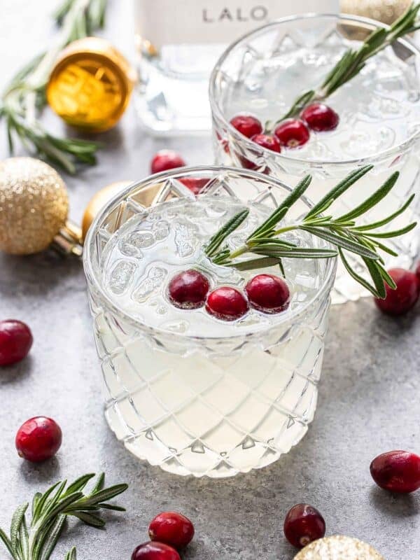 White cranberry christmas margarita in a glass garnished with a sprig of rosemary and fresh cranberries.
