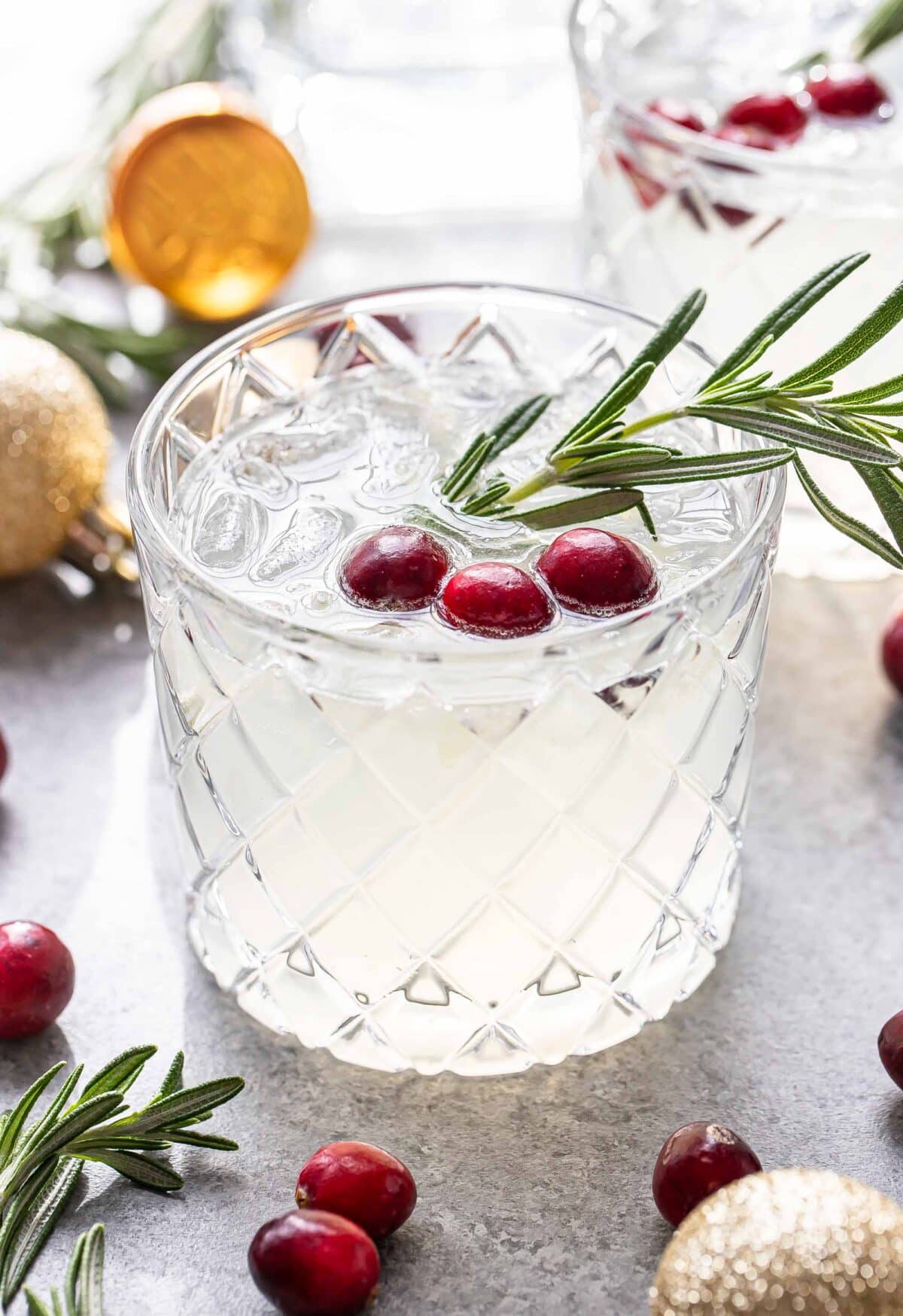 White Christmas margarita in a glass garnished with a sprig of rosemary and fresh cranberries.
