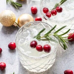 Two Christmas margaritas garnished with a sprig of rosemary and fresh cranberries.
