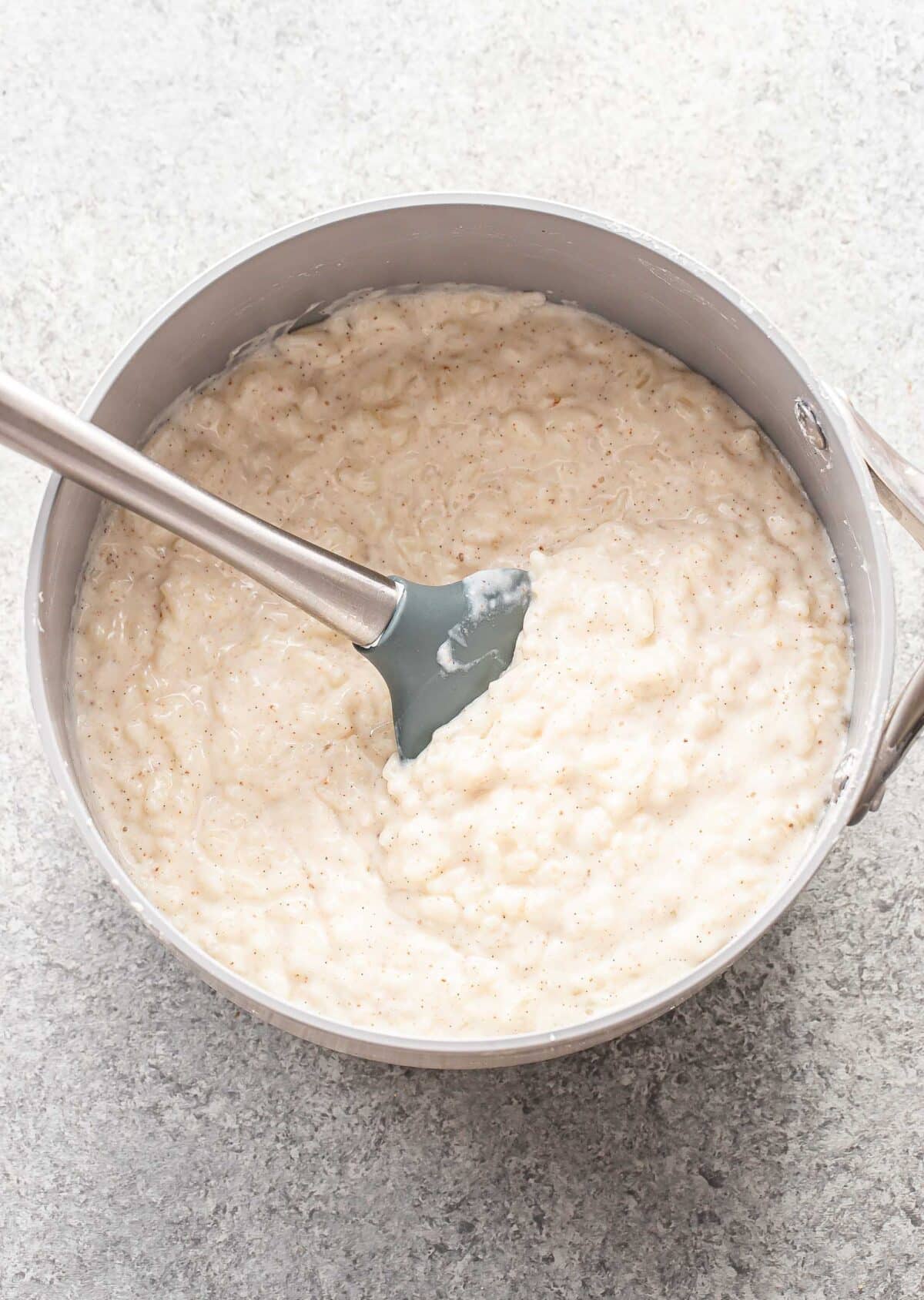 Rice pudding in a saucepan with a rubber spatula.
