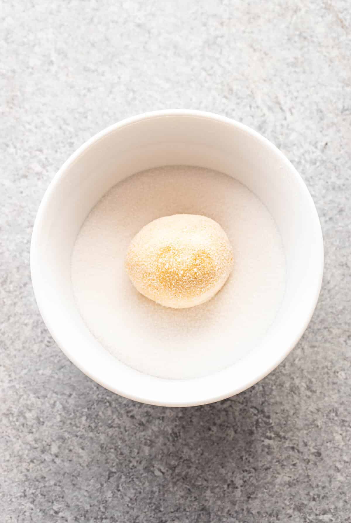Sugar cookie dough ball in a white bowl with sugar.