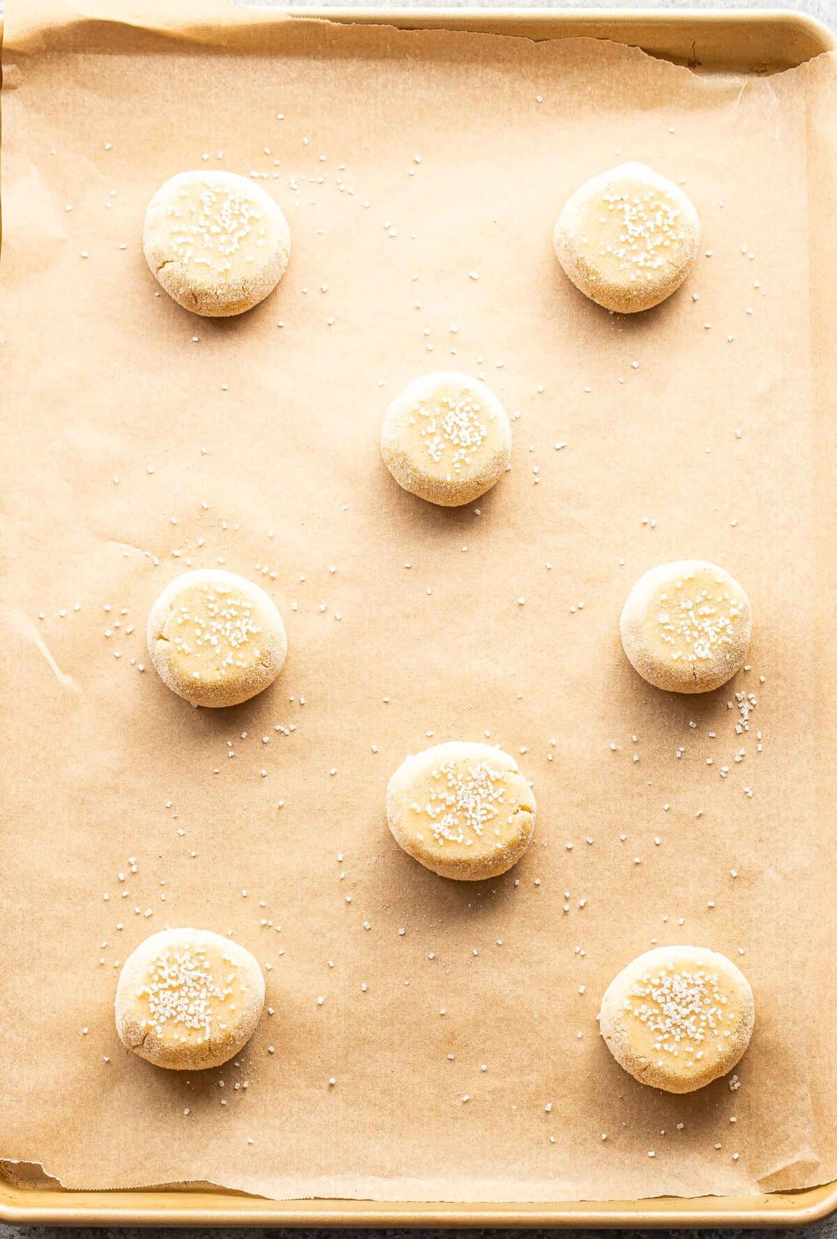 Unbaked sugar cookies on a parchment paper lined baking sheet.