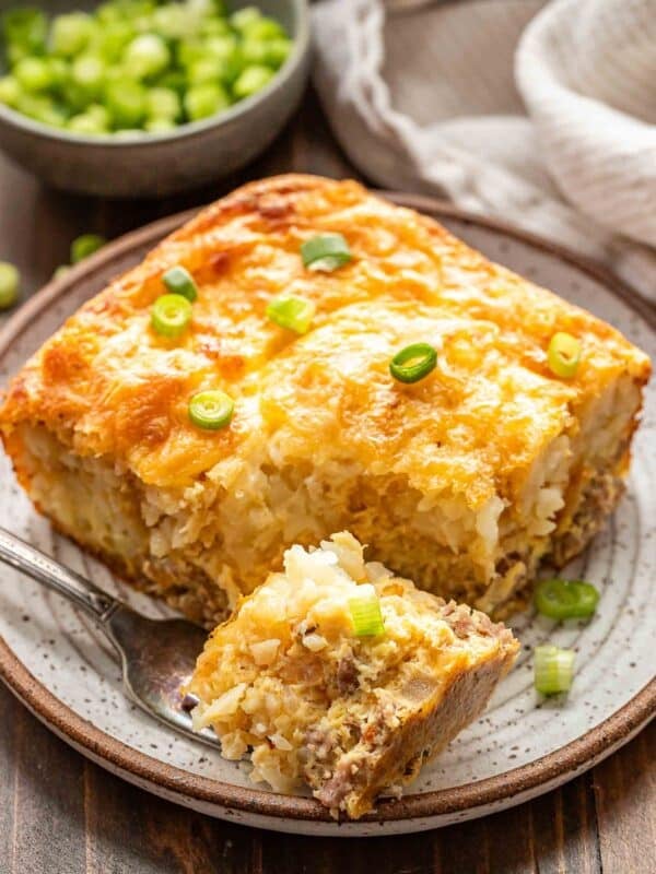 A piece of tater tot breakfast casserole on a white plate with a piece cut off and resting on a fork.