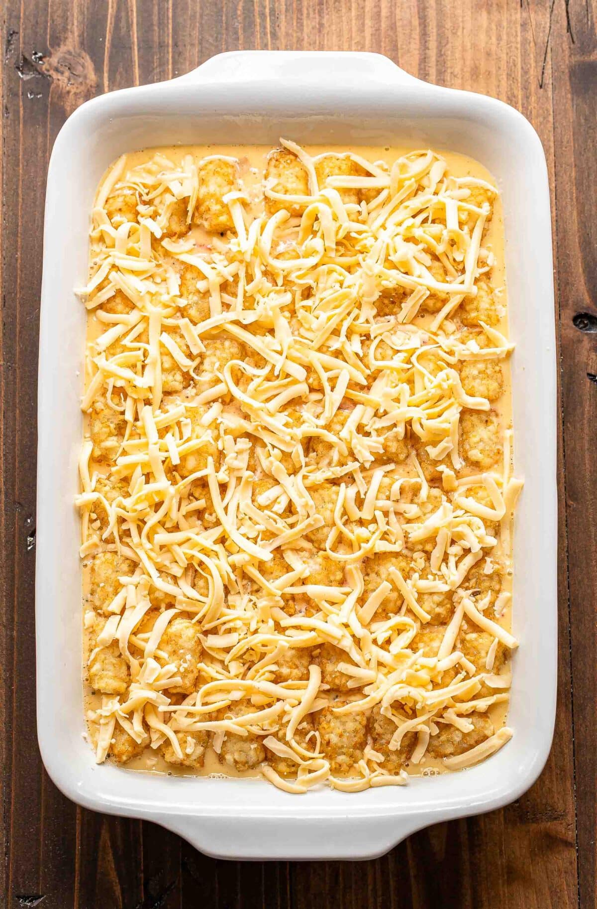 tater tot and egg breakfast casserole in a casserole dish topped with cheese before it's been baked.