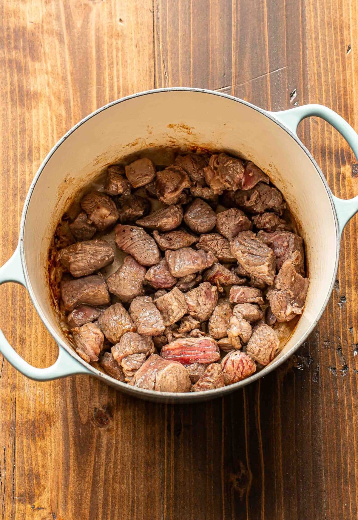 Stew meat partially cooked in a pot.