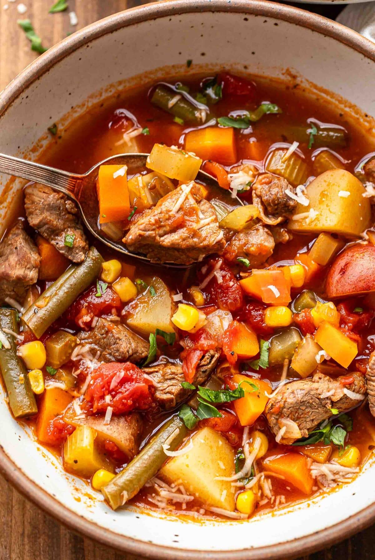 Vegetable beef soup in a white bowl with a spoon holding up some of it.