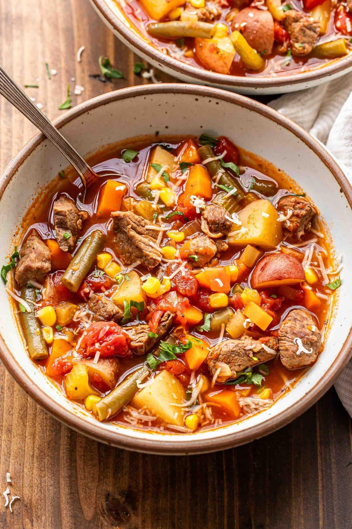 Beef soup with potatoes, green beans, corn, and tomatoes in a white bowl with a spoon.