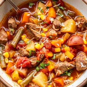 Beef, potato, and vegetable soup in a white bowl with a spoon.