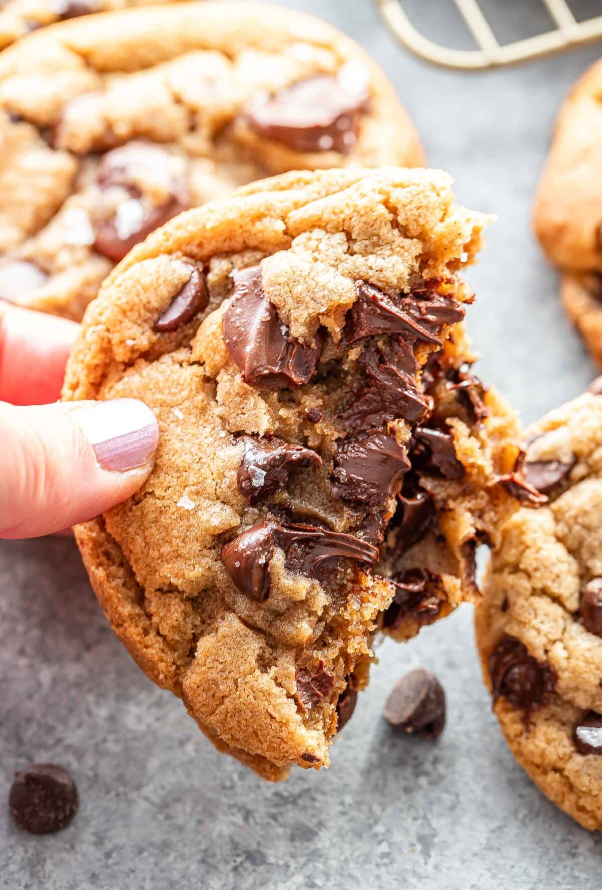 Hand holding a chocolate chip cookie that's broken in half.