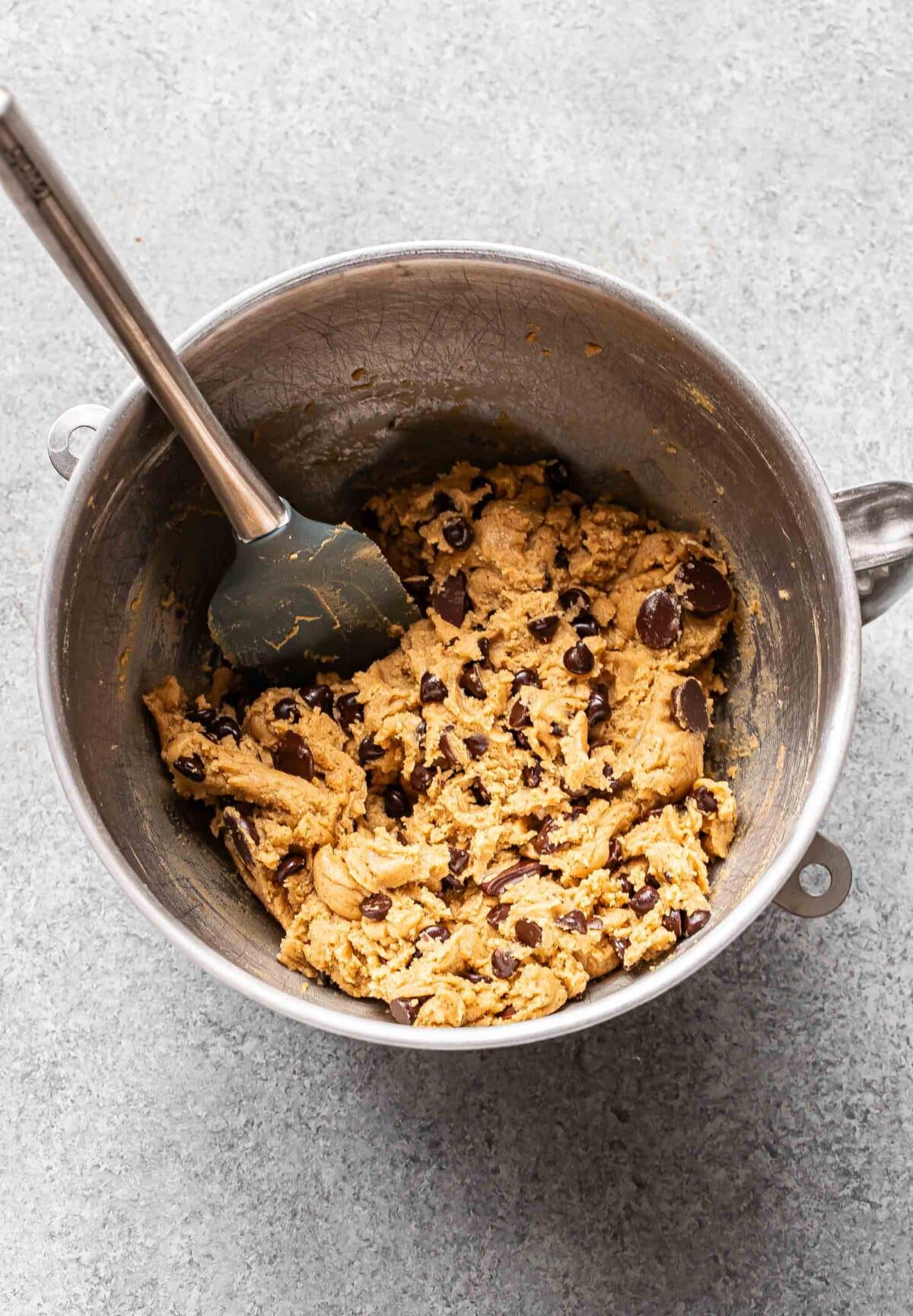 Chocolate chip cookie dough in a mixing bowl with a rubber spatula.
