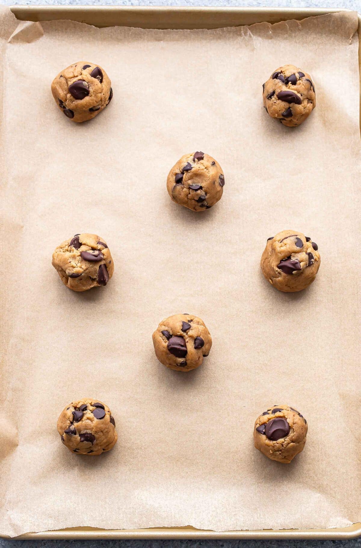 Chocolate chip cookie dough balls on a parchment paper lined baking pan.