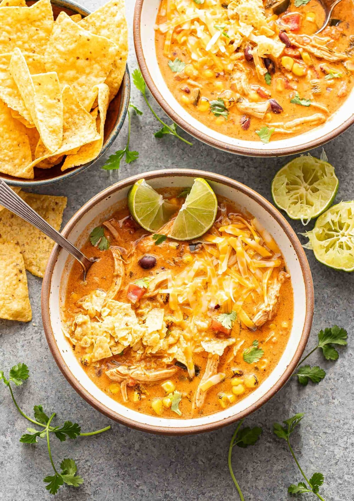 Two white bowls filled with creamy chicken tortilla soup. The soup is topped with cheese and crushed tortilla chips.