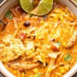 A bowl of creamy chicken tortilla soup topped with melted cheese, tortilla chips, and a lime wedge.