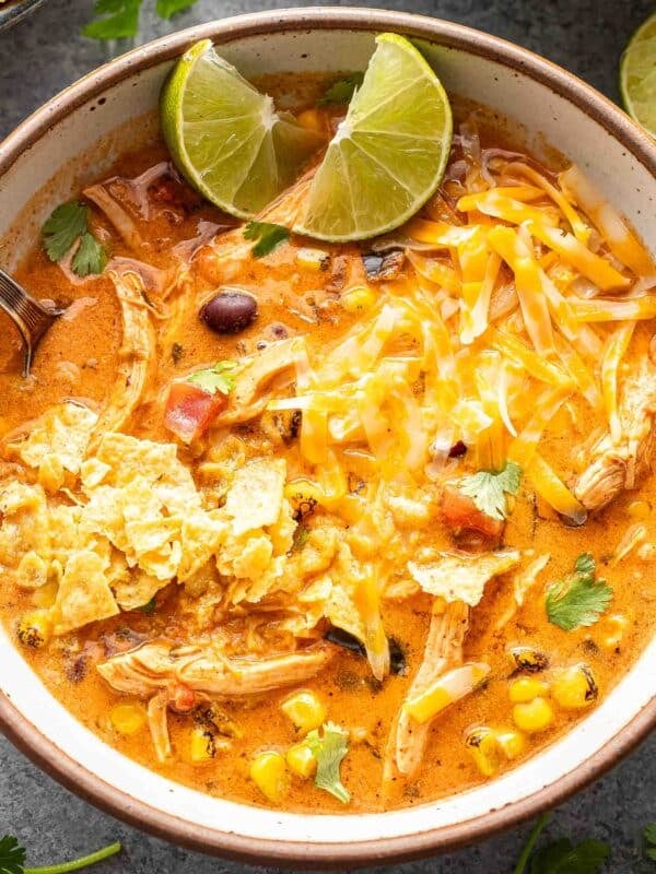 A bowl of creamy chicken tortilla soup topped with melted cheese, tortilla chips, and a lime wedge.
