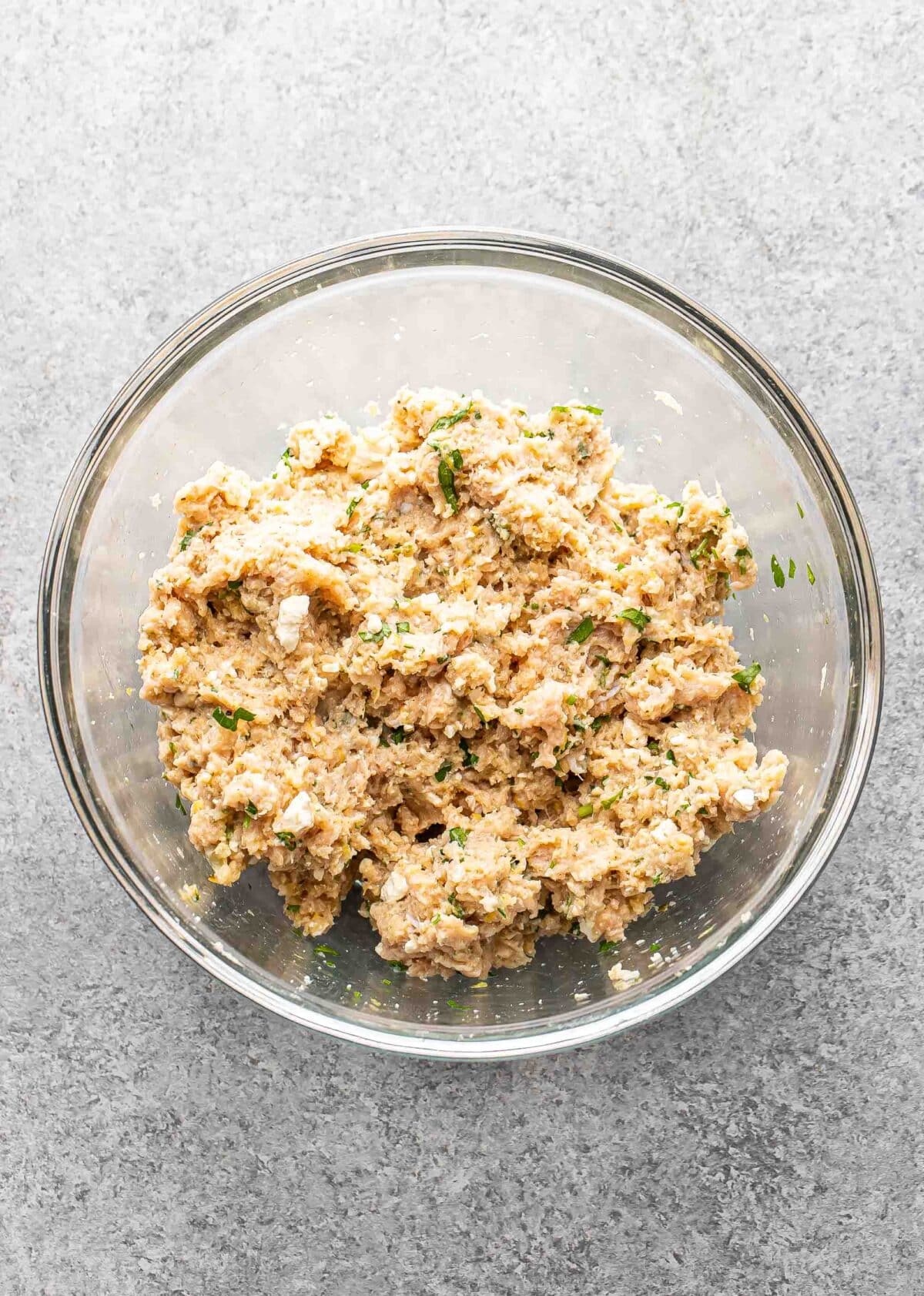 Greek chicken meatball mixture in a glass mixing bowl.