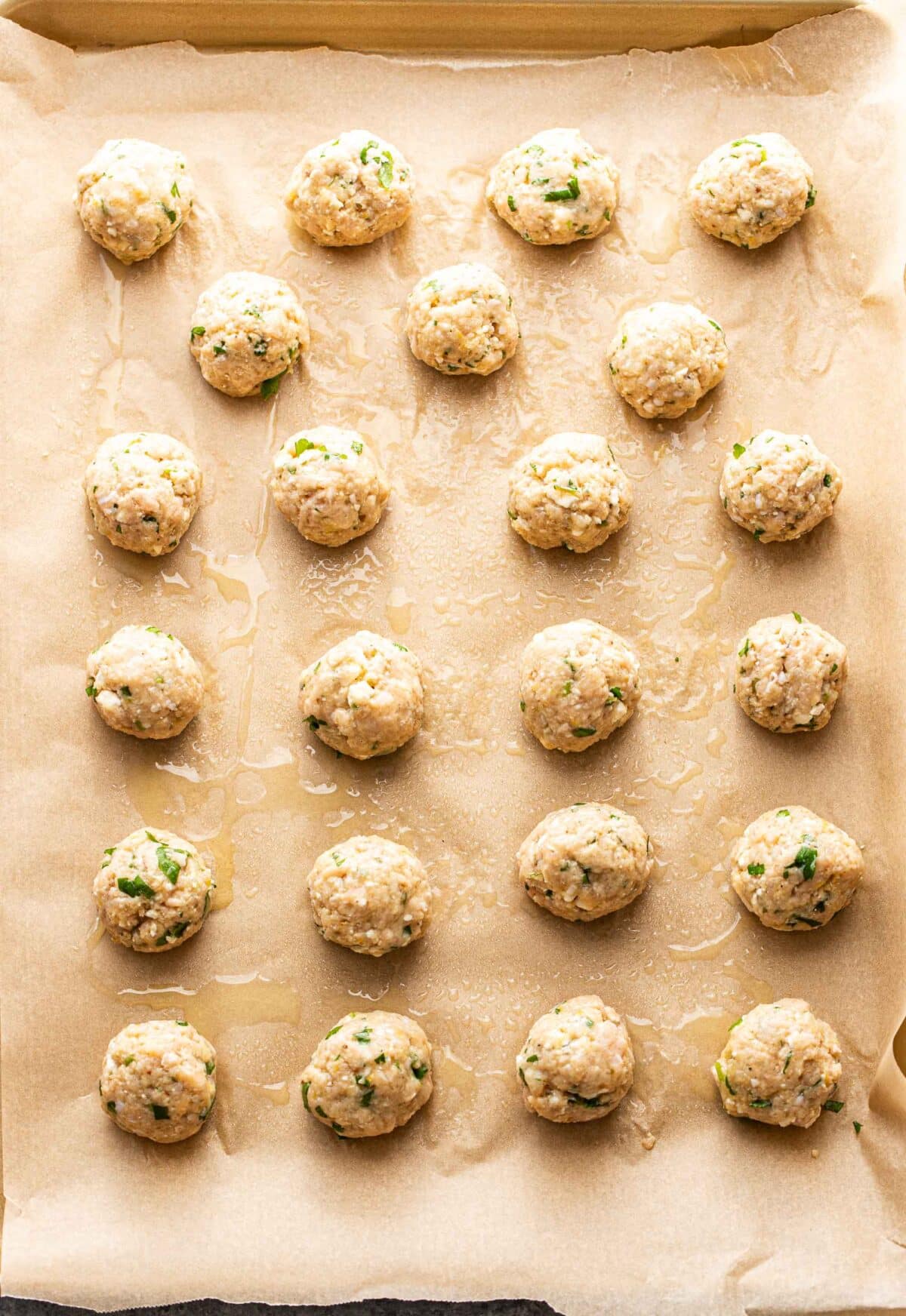 Greek chicken meatballs on a parchment paper lined baking sheet before being baked.
