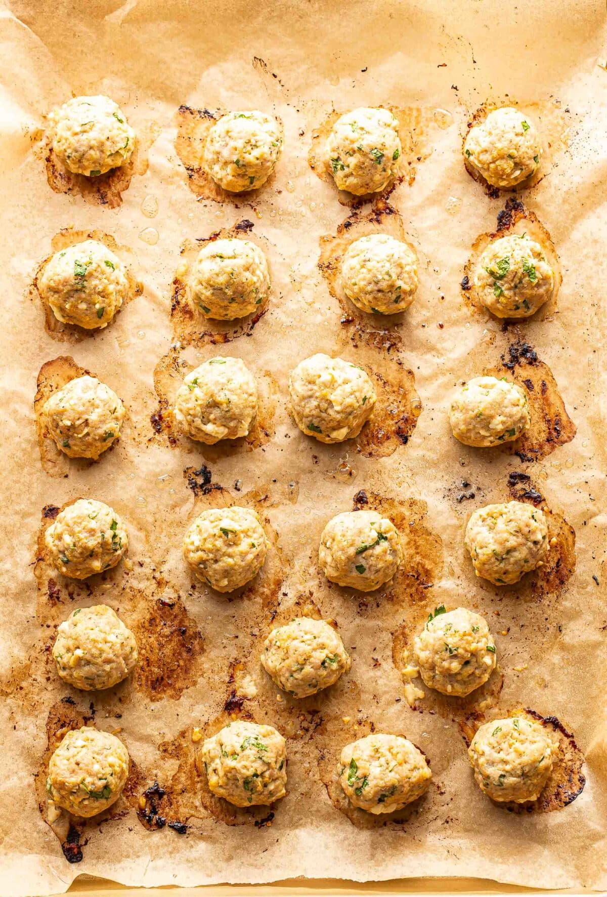 Baked Greek chicken meatballs on a parchment paper lined baking sheet.