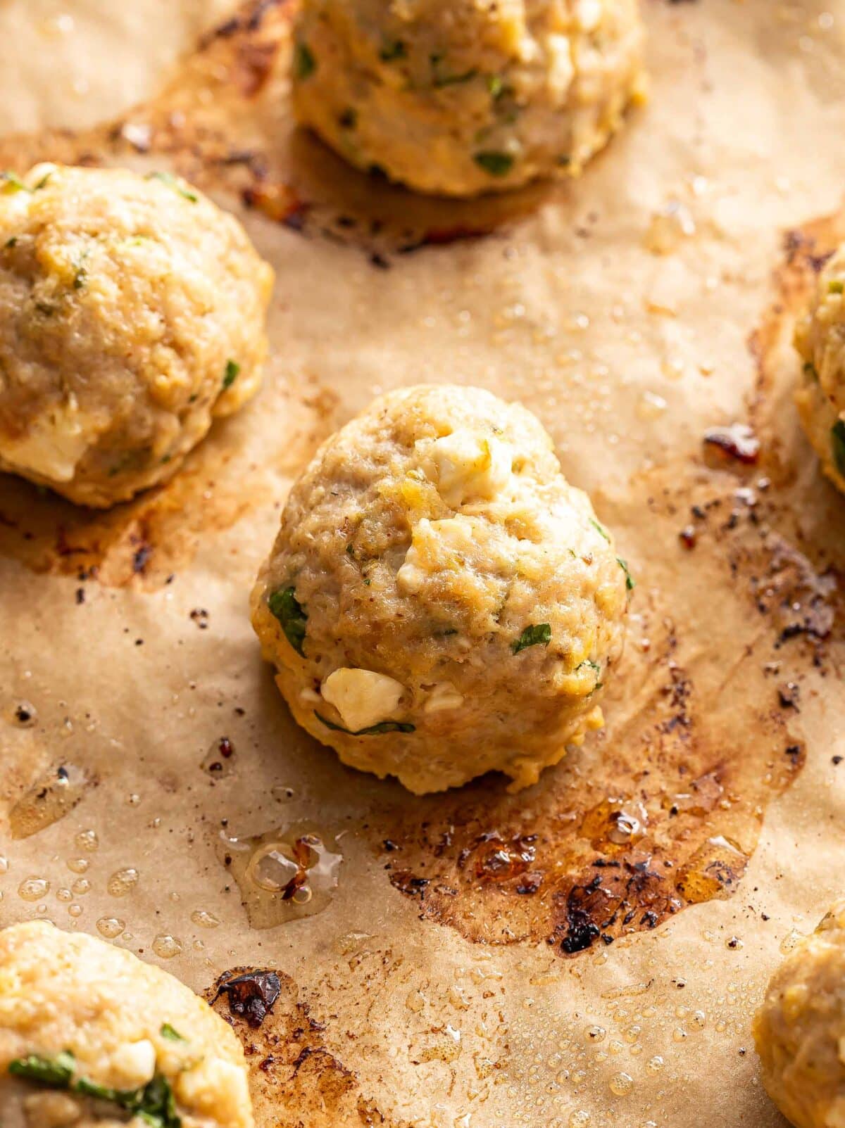 Baked Greek chicken meatball on a parchment paper lined baking sheet.