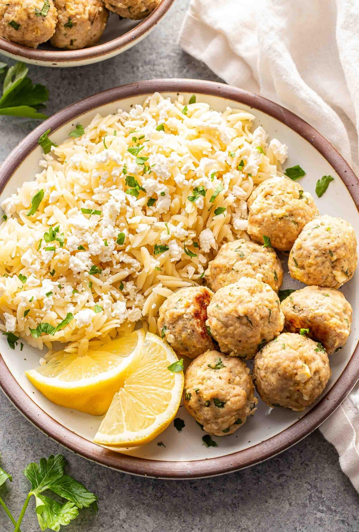 Greek chicken meatballs on a white plate with orzo and lemon wedges.