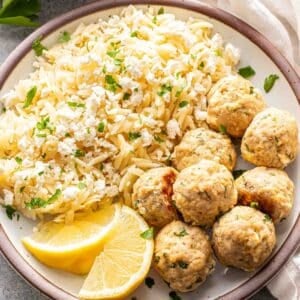 Greek chicken meatballs on a white plate with orzo and lemon wedges.