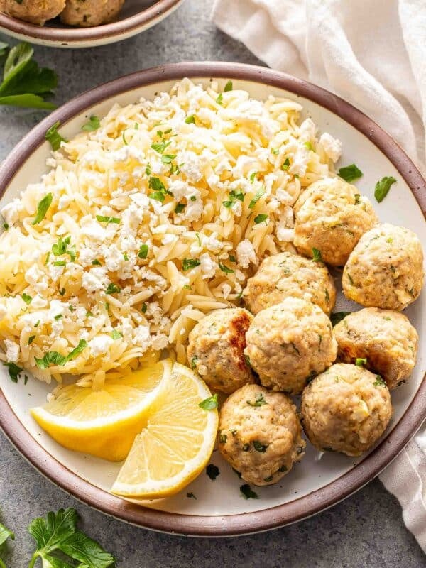 Greek chicken meatballs on a white plate with orzo and lemon wedges.
