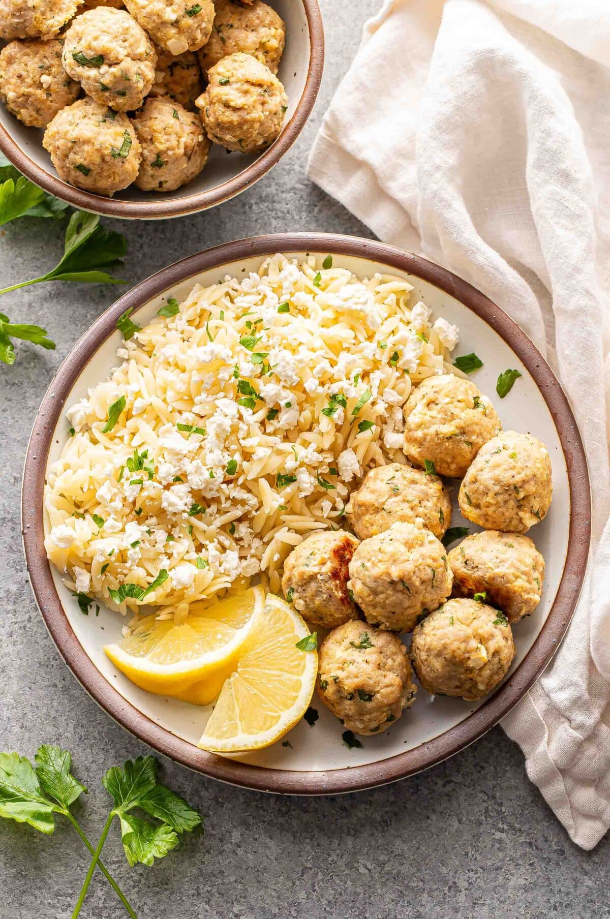 Greek chicken meatballs on a white plate with orzo and lemon wedges.