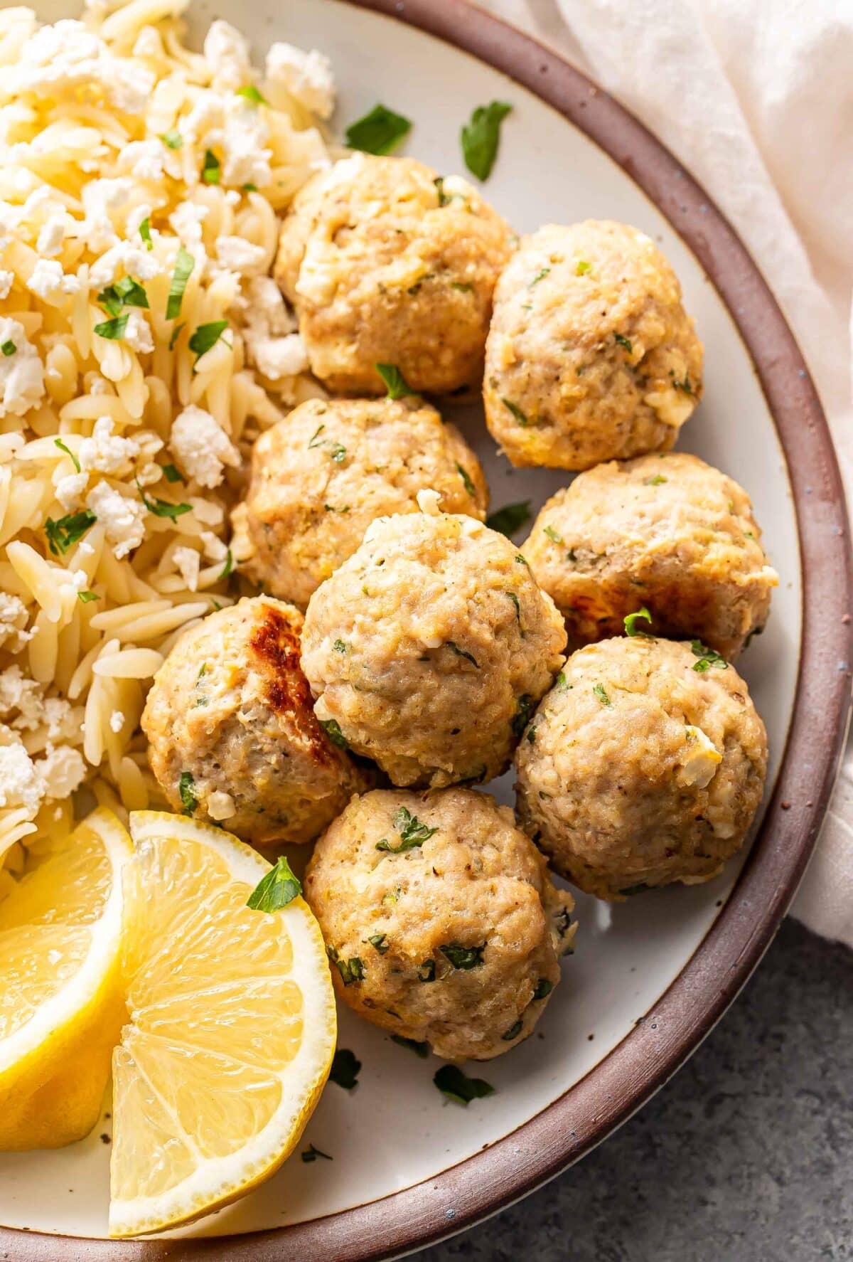 Greek chicken meatballs on a white plate with lemon wedges.