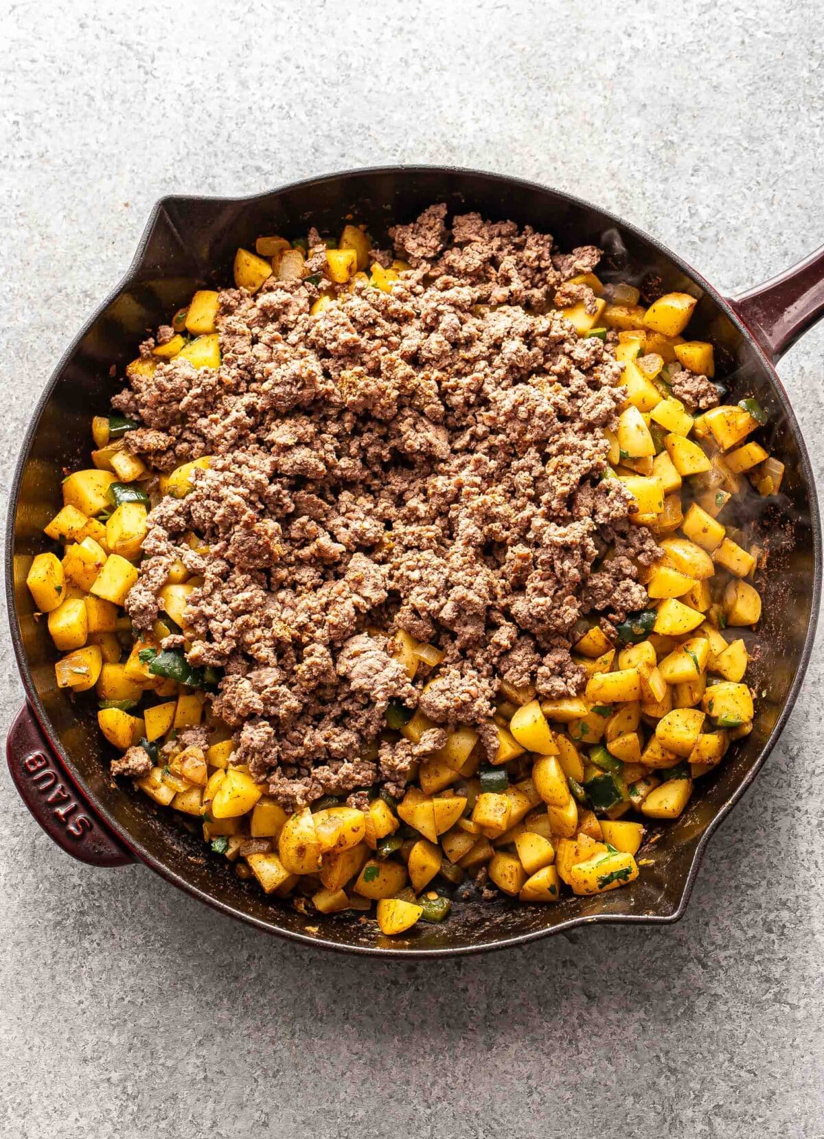 Cooked diced potatoes and ground beef in a skillet.
