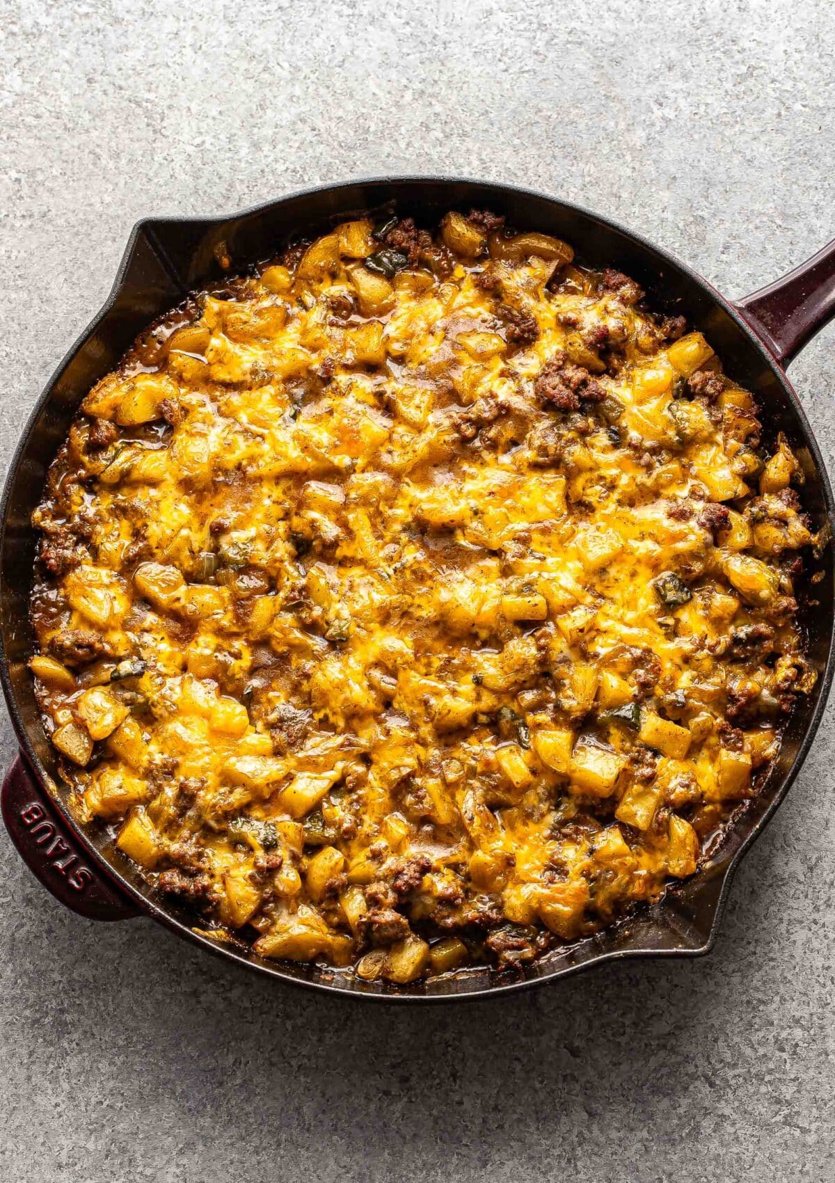 Ground beef potato casserole topped with melted cheese in a skillet.