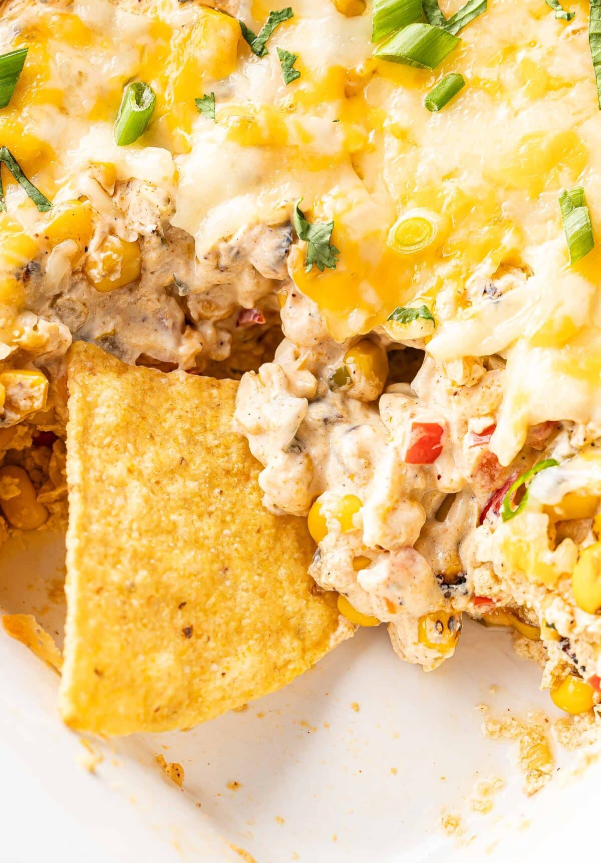 Tortilla chip in the white casserole dish with the baked corn dip.