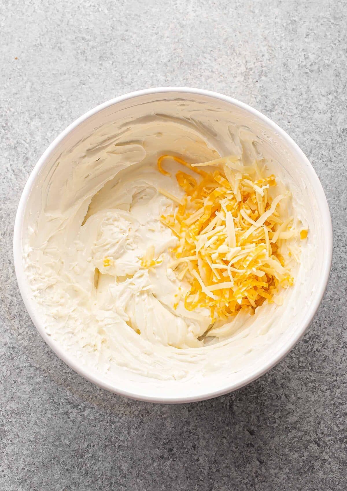 Creamy cheese, Greek yogurt, and shredded cheese in a white mixing bowl.