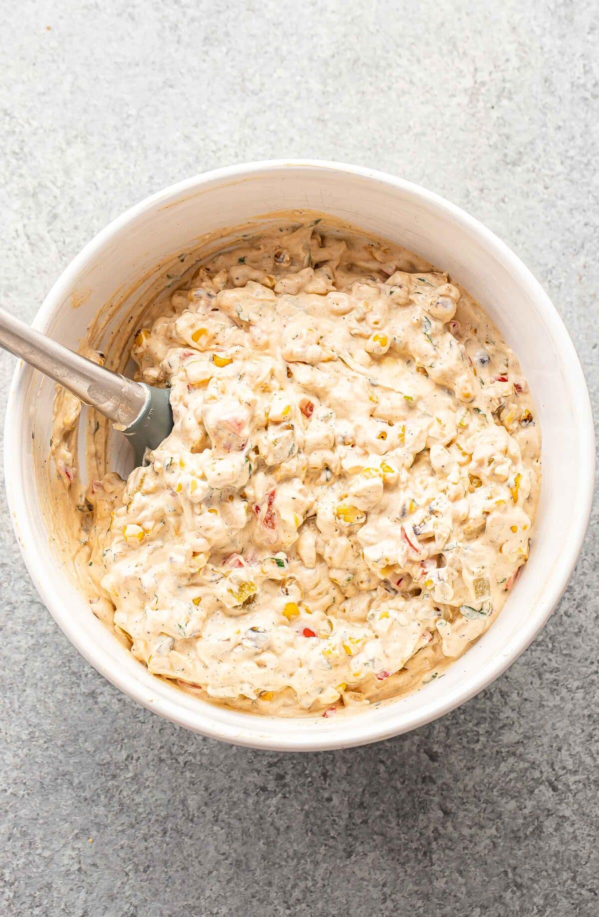 Corn dip mixture in a white mixing bowl with a rubber spatula.