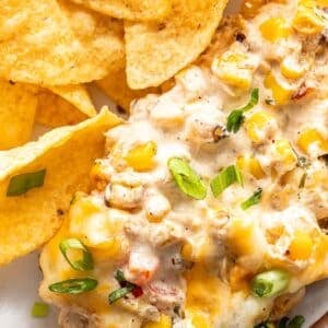 Creamy baked corn dip on a white plate with tortilla chips.