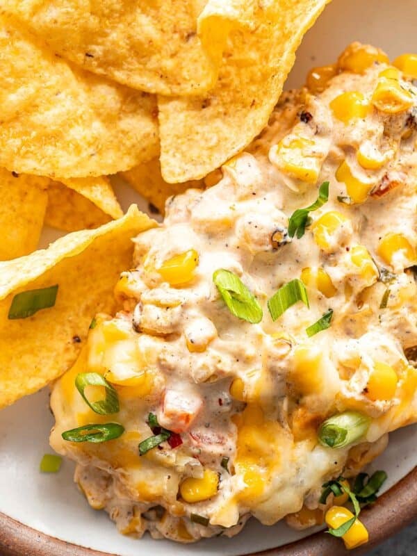 Creamy baked corn dip on a white plate with tortilla chips.